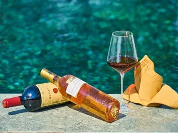 two wine bottles and a glass of wine next to a pool of water